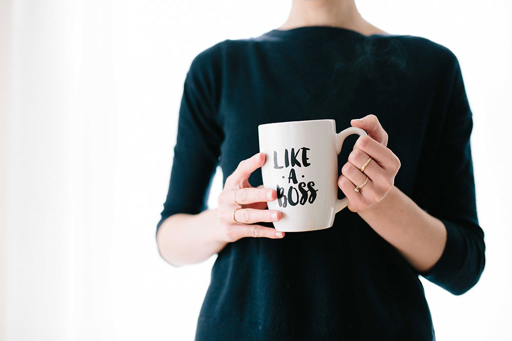 Woman in long sleeve black shirt holding a mug that says Like A Boss.