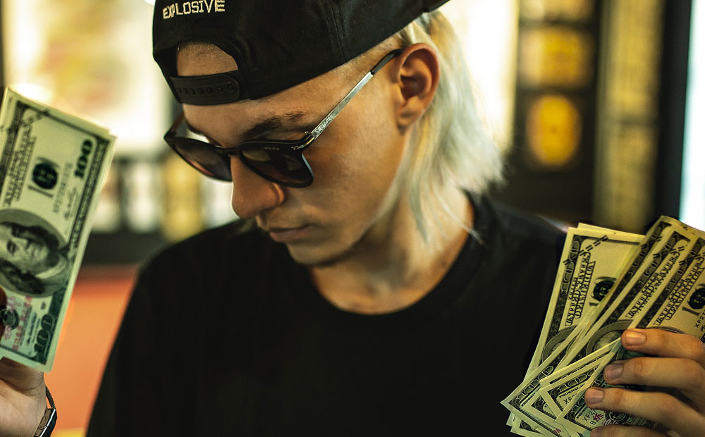 Blonde man with backwards hat and sunglasses holding money