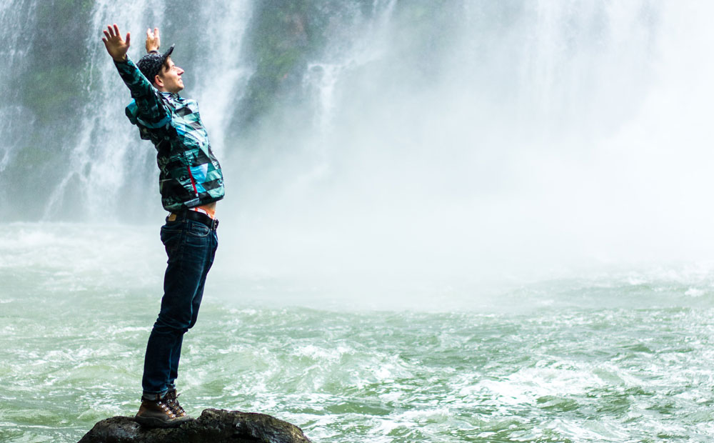 man standing on black rock surrounded body of water